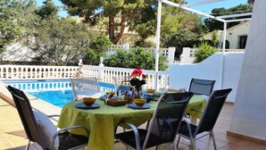 A poolside dining area with a table set for two, surrounded by chairs, and a pool in the background. - Villa Zsara very near La Fustera In its own grounds with private pool (Calp)