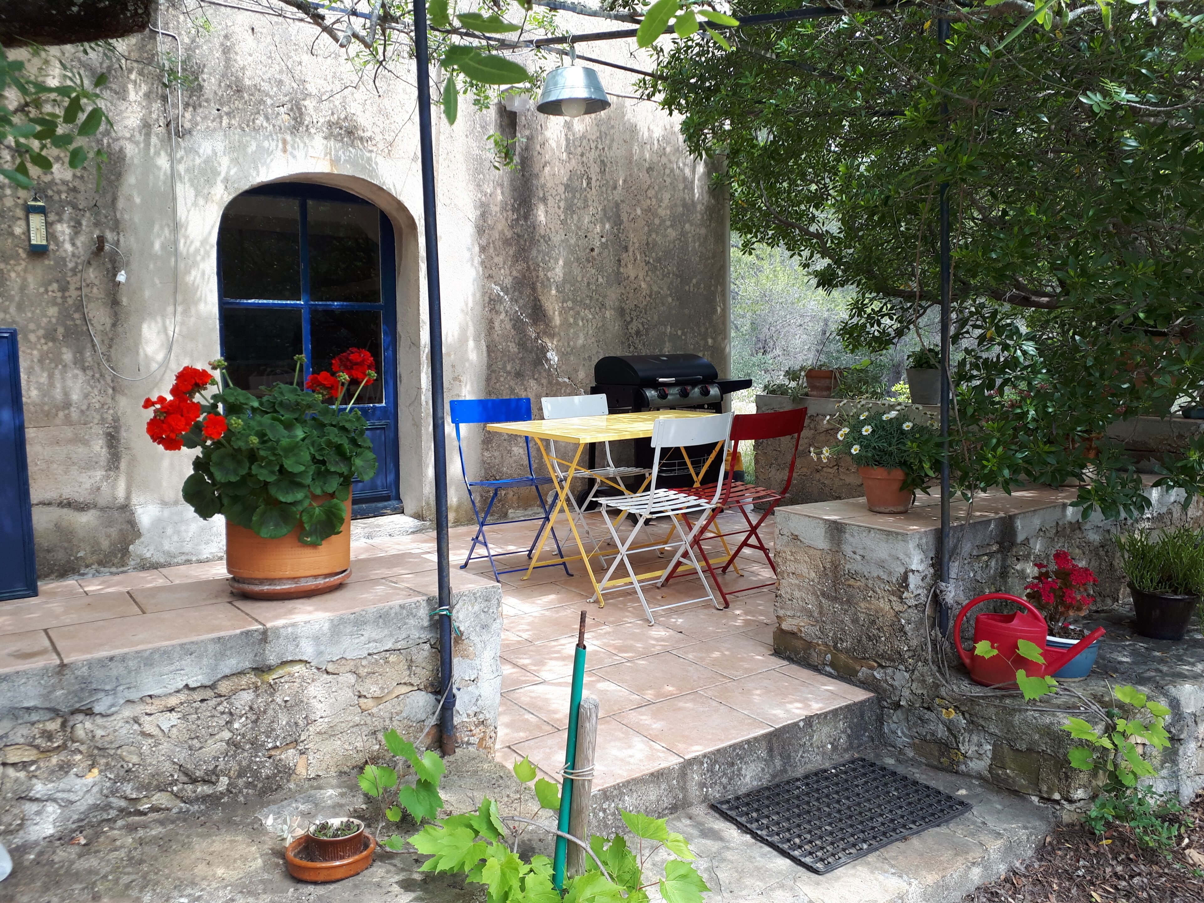 A patio with a table and chairs, a grill, and potted plants.