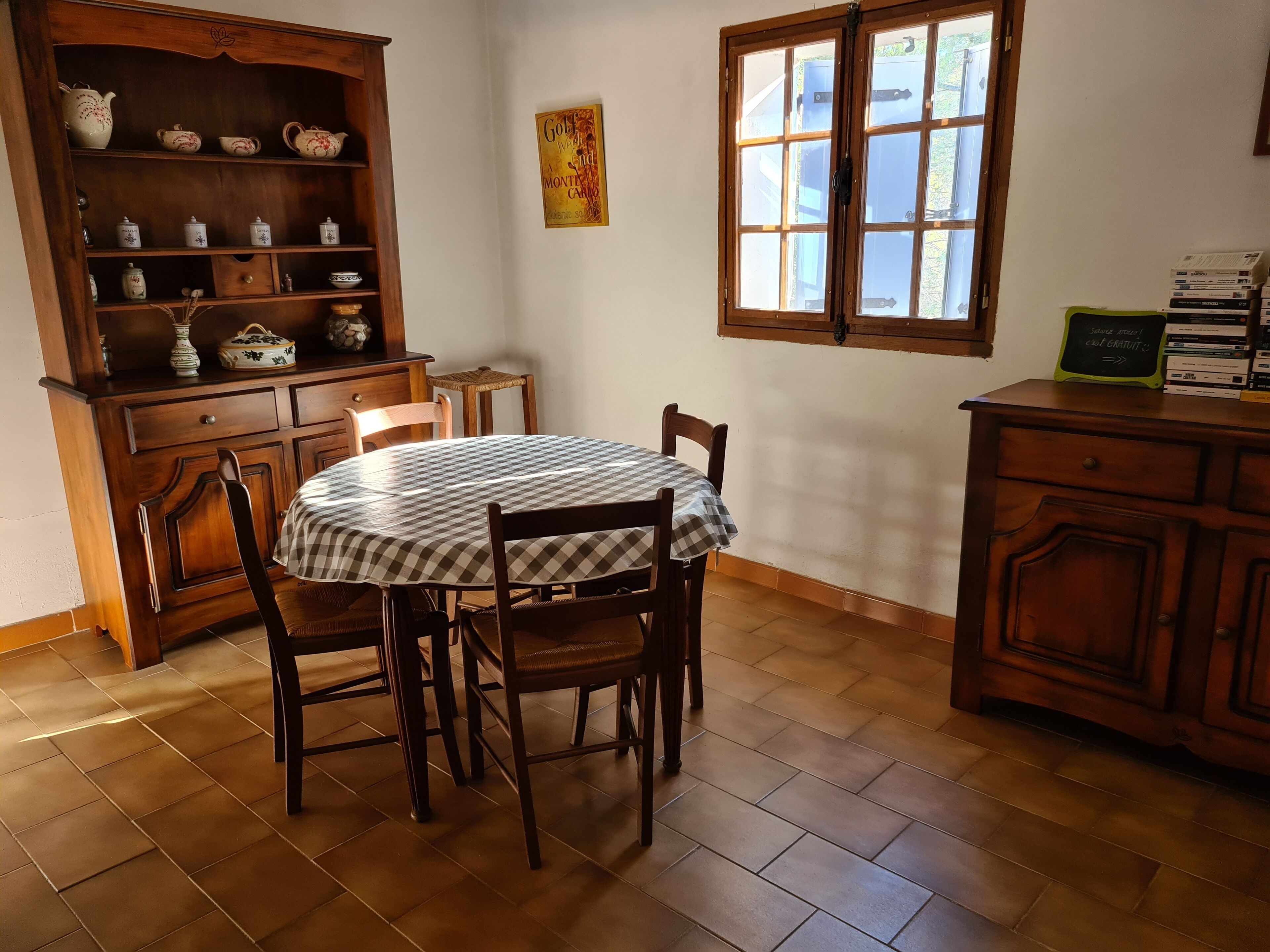 A dining area with a round table, chairs, a wooden cabinet with shelves, a window, and a wall-mounted picture.