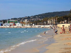 A beach with people, a clear sky, and buildings in the background.