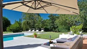 Un espace aménagé au bord de la piscine, comprenant une chaise longue, un canapé et un grand parasol.