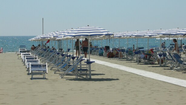 Une plage bordée de rangées de transats et d’ombrelles à rayures bleues et blanches.