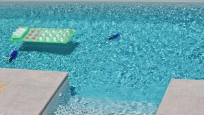 Une piscine d’un bleu éclatant, avec un bar flottant et deux chaises longues bleues.