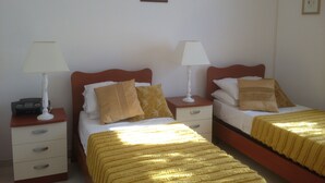 A hotel room with two single beds, each with a bedside table, a lamp, and a decorative pillow. - Spacious, modern ground floor apartment, private patio and garden, mosquito nets (Calabria)
