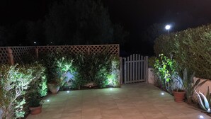 A well-lit patio area with tiled flooring, potted plants, and a wooden fence. - Spacious, modern ground floor apartment, private patio and garden, mosquito nets (Calabria)