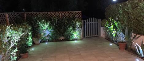 A well-lit patio area with tiled flooring, potted plants, and a wooden fence.