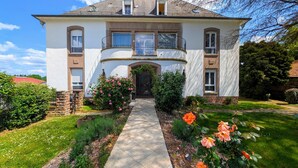 A two-story house with a central entrance, a balcony on the upper floor, and a well-maintained garden with flowers and shrubs. - Domaine La Rosière - Villa for 50 people Indoor swimming pool, Tennis court, Cinema, etc. (Diemeringen)