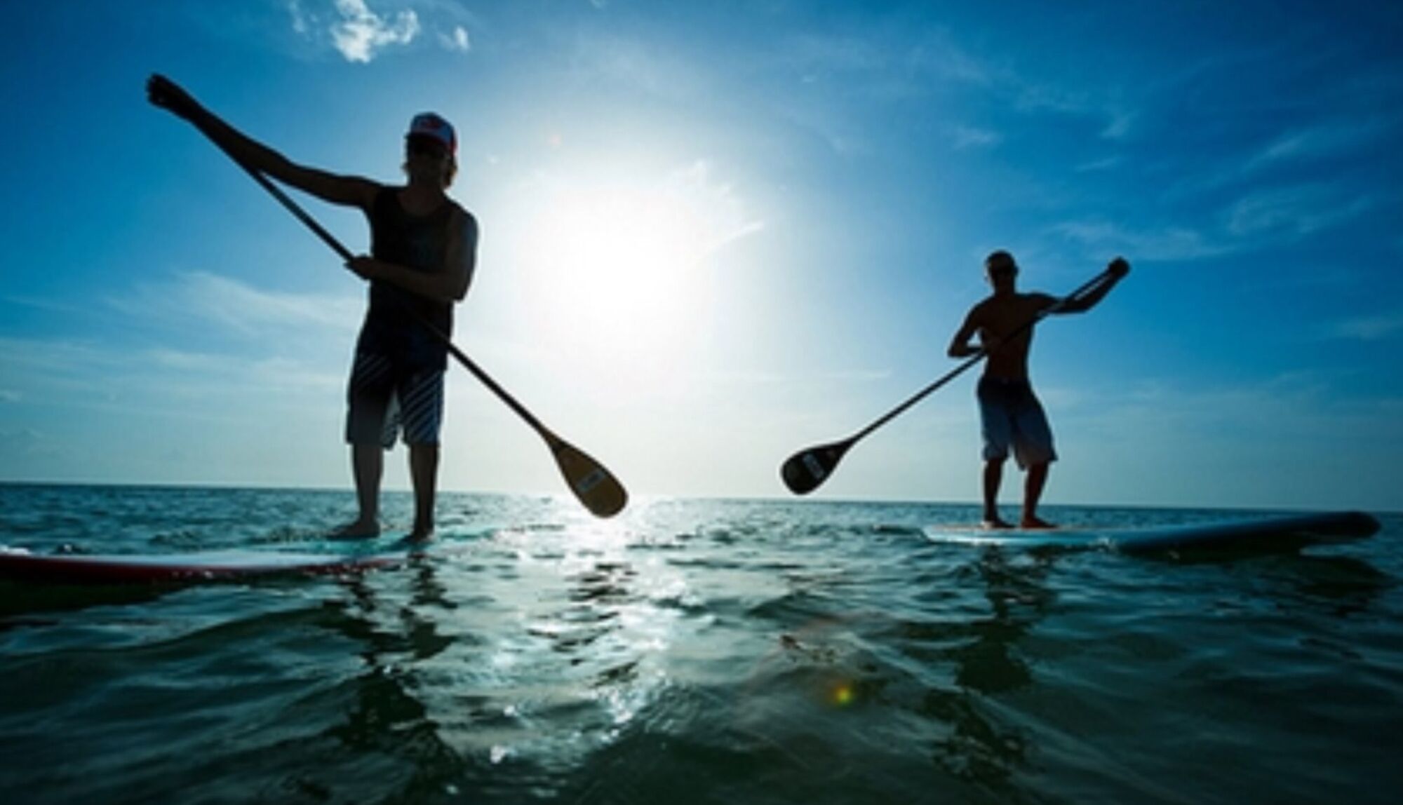 Two people paddleboarding on a calm sea with the sun low on the horizon.