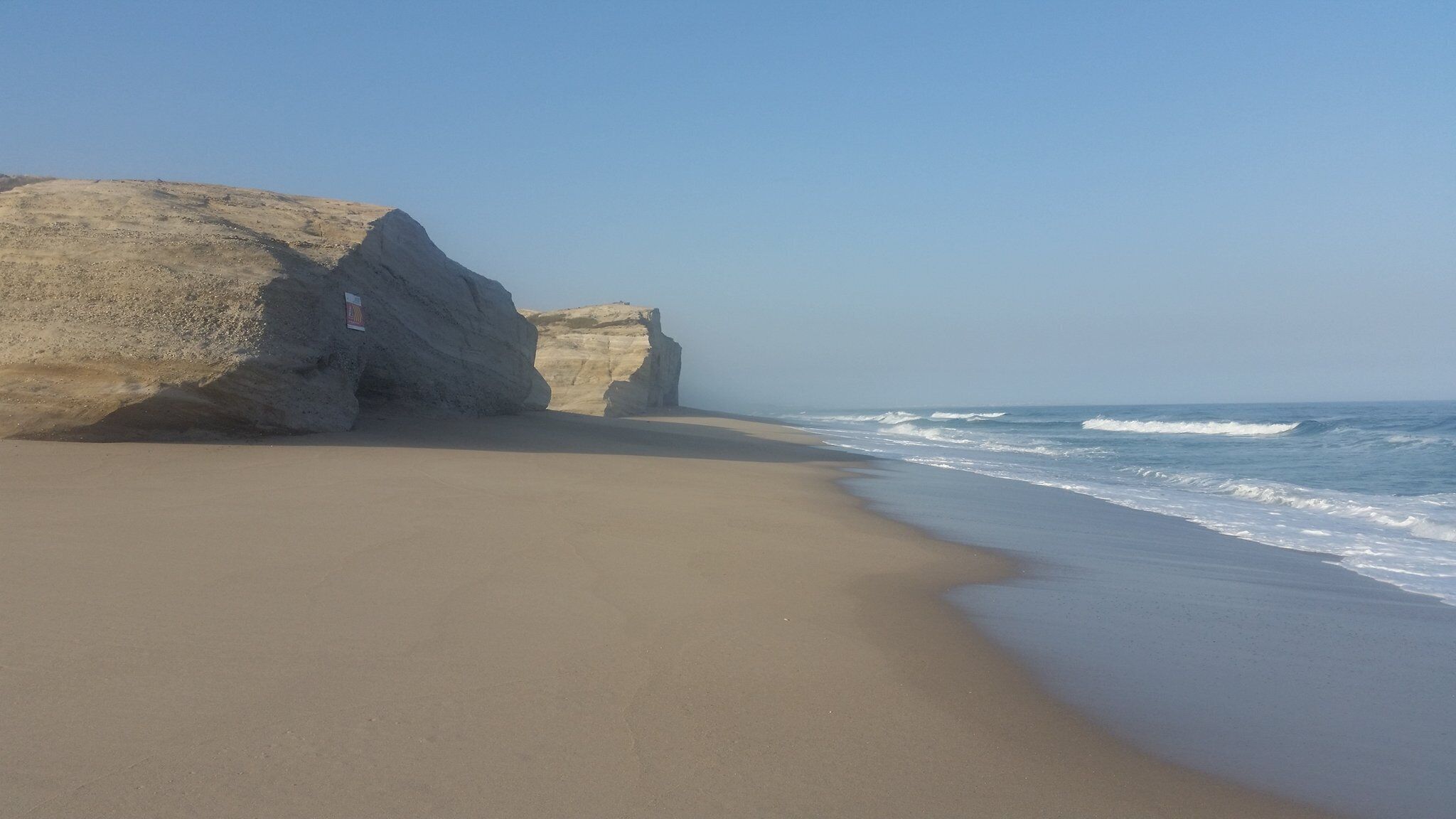 Une plage avec une grande formation rocheuse et des vagues déferlantes.