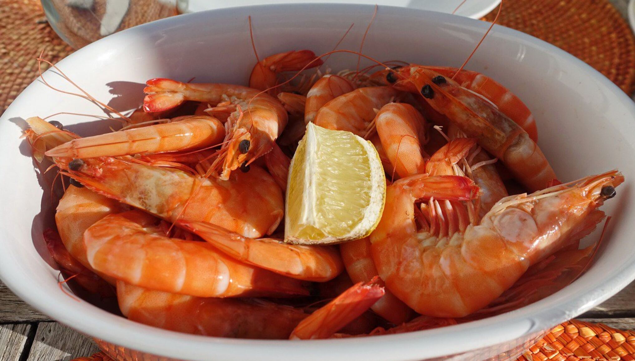 A bowl of cooked shrimp with a lemon wedge.