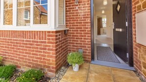 Une façade en briques avec une porte, une petite plante en pot et une fenêtre donnant sur la maison voisine.