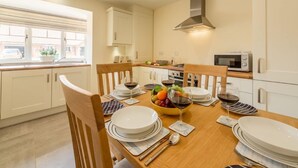 Une cuisine moderne avec des meubles blancs, une table à manger en bois pour quatre personnes et un panier de fruits posé sur la table.