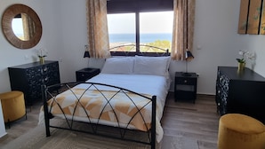 A bedroom with a bed, bedside tables, a dresser, a mirror, and a view of the sea. - Luxury Detached Villa With Private Pool And Views Over The Sea (Afandou)
