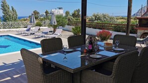 A poolside area with a dining table, lounge chairs, and a view of the sea. - Luxury Detached Villa With Private Pool And Views Over The Sea (Afandou)