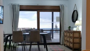 A dining area with a table and chairs, a wooden cabinet, and a view through large windows. - Luxury Detached Villa With Private Pool And Views Over The Sea (Afandou)
