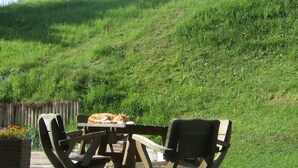 Una mesa de picnic con sillas en una colina cubierta de césped, con montañas al fondo.