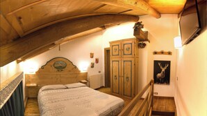 Un dormitorio con techo de madera, una cama con ropa de cama estampada, un armario de madera, un radiador y un cuadro de un ciervo.
