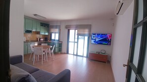 En moderne stue med et fladskærms-tv, et spiseområde med bord og stole, og et køkken med grønne skabe.