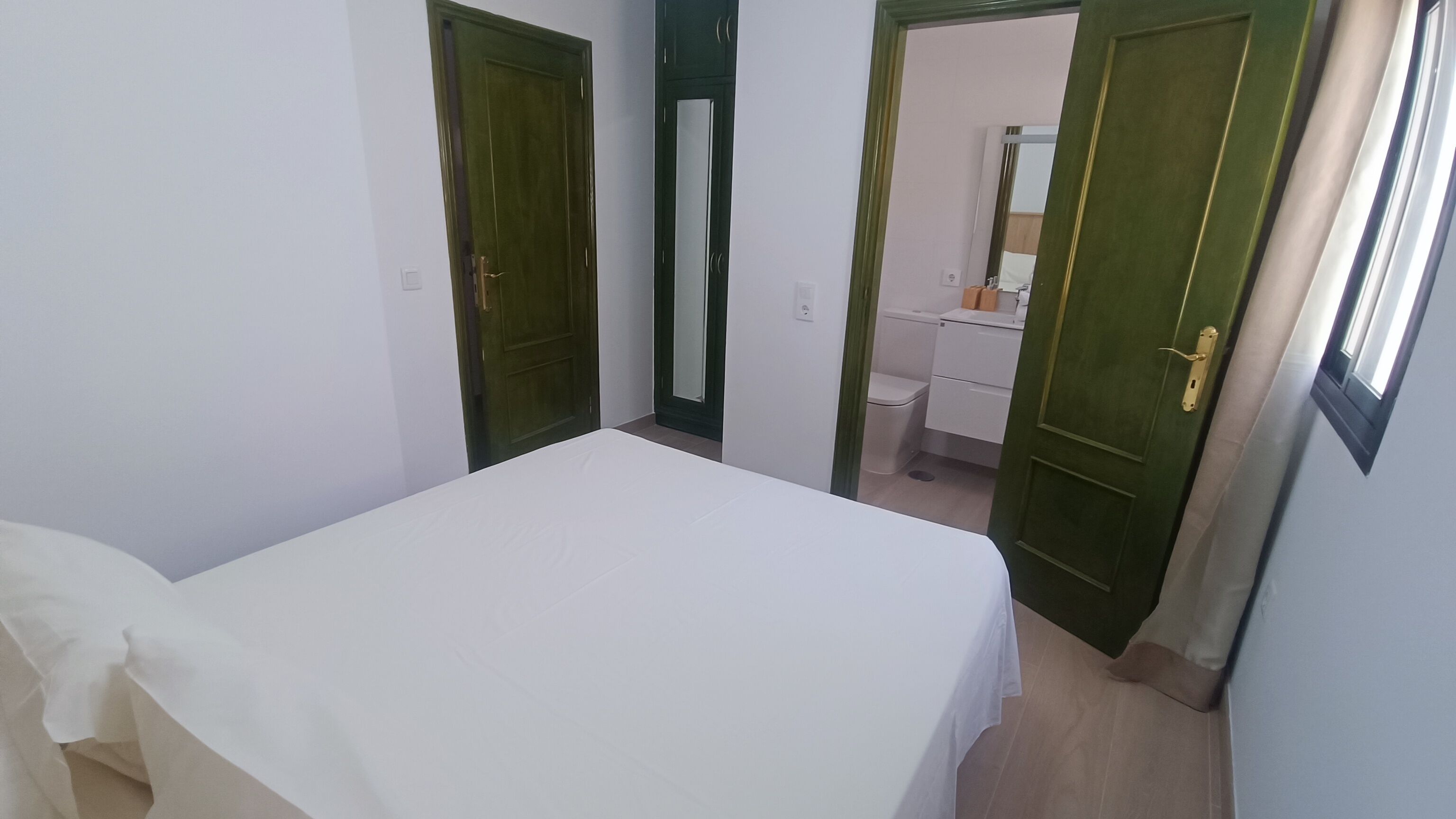 Un dormitorio con cama, dos puertas y un baño visible a través de una puerta abierta.