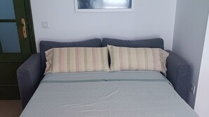 Ein Bett mit weißer Matratze und gestreifter Bettwäsche, ein Holzboden und eine Tür mit grünem Rahmen.