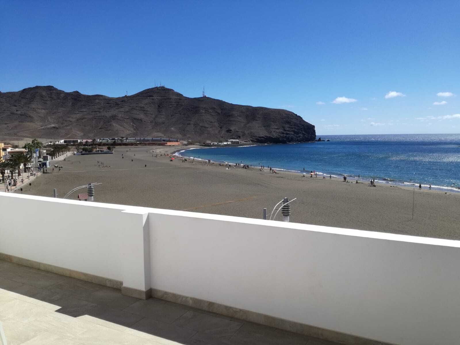 Une plage avec une falaise rocheuse en arrière-plan, un ciel dégagé et une vue sur l’océan.