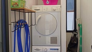 Een kleine wasruimte met een Bosch wasmachine en droger, een boiler en een klein raam.