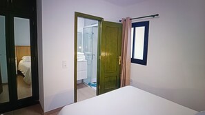 Une pièce comprenant un lit, une porte donnant sur une salle de bain et une fenêtre avec un rideau.