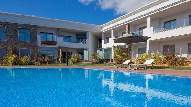 A modern hotel with a swimming pool, sun loungers, and a clear blue sky.