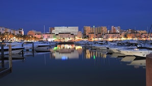 A marina with boats docked, reflecting city buildings and palm trees in the background.