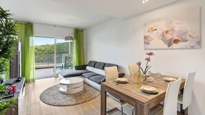 A modern living room with a sofa, coffee table, dining table set for two, and a balcony with a view.