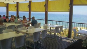 An outdoor dining area with tables and chairs, overlooking the sea.