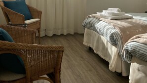 Una habitación con una cama, dos sillones de mimbre, una ventana con cortinas translúcidas y un adorno en la pared.