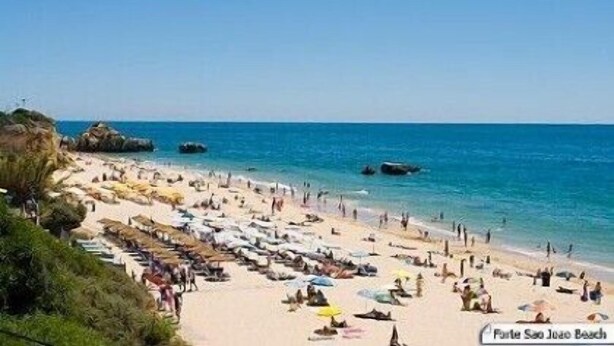 Una spiaggia con persone che prendono il sole e nuotano, e un cielo blu limpido.
