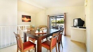 Zona pranzo con tavolo e sedie, televisore su un mobile e un quadro appeso al muro.