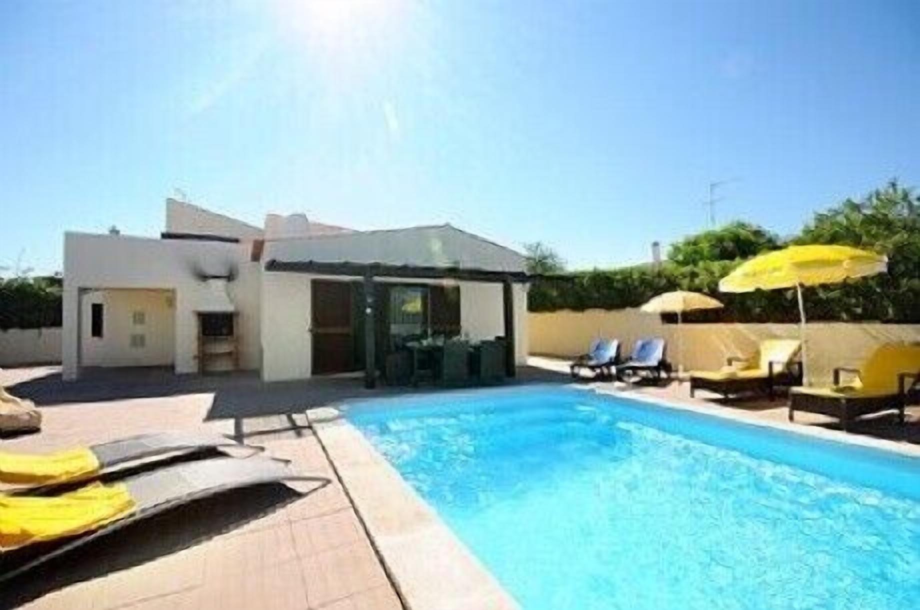A modern pool area with a clear blue pool, sun loungers, and umbrellas.