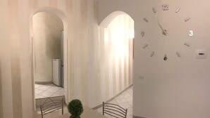Ein Flur mit einer Uhr an der Wand, einer kleinen Pflanze und einer Treppe mit einem Stuhl.