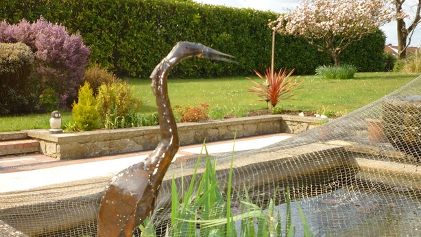 A bird statue in a garden with a pond, surrounded by greenery and a hedge. - Accessible Holiday Let In Secluded Location (Beacon Hill)