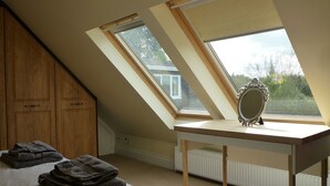 A bedroom with a sloped ceiling, skylights, a wooden wardrobe, a bedside table with a mirror, and a radiator. - Accessible Holiday Let In Secluded Location (Beacon Hill)