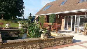 A patio area with a brick house, a small pond, and outdoor furniture. - Accessible Holiday Let In Secluded Location (Beacon Hill)