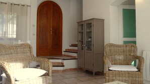 Quarto com cadeiras de vime, porta de madeira, armário e piso de azulejos.