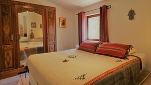 Quarto com cama grande, guarda-roupa de madeira e janela com cortinas.