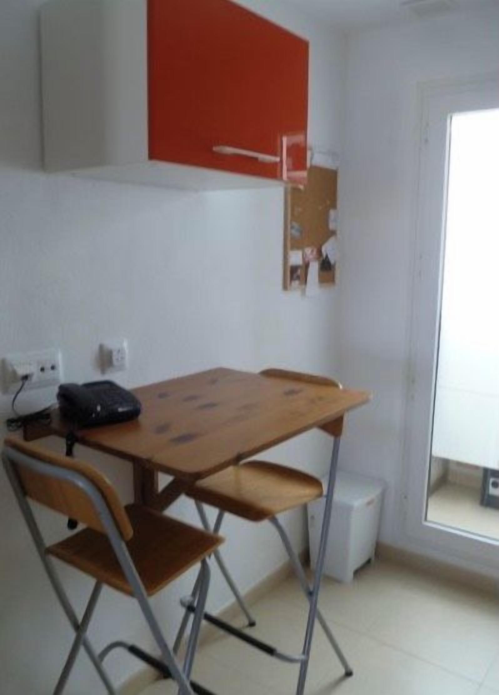 Une petite pièce simple, avec une table en bois et deux chaises, un buffet rouge et une porte blanche.