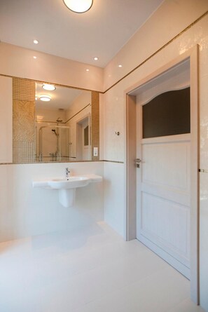 Un baño con un lavamanos blanco, un espejo grande y una puerta.