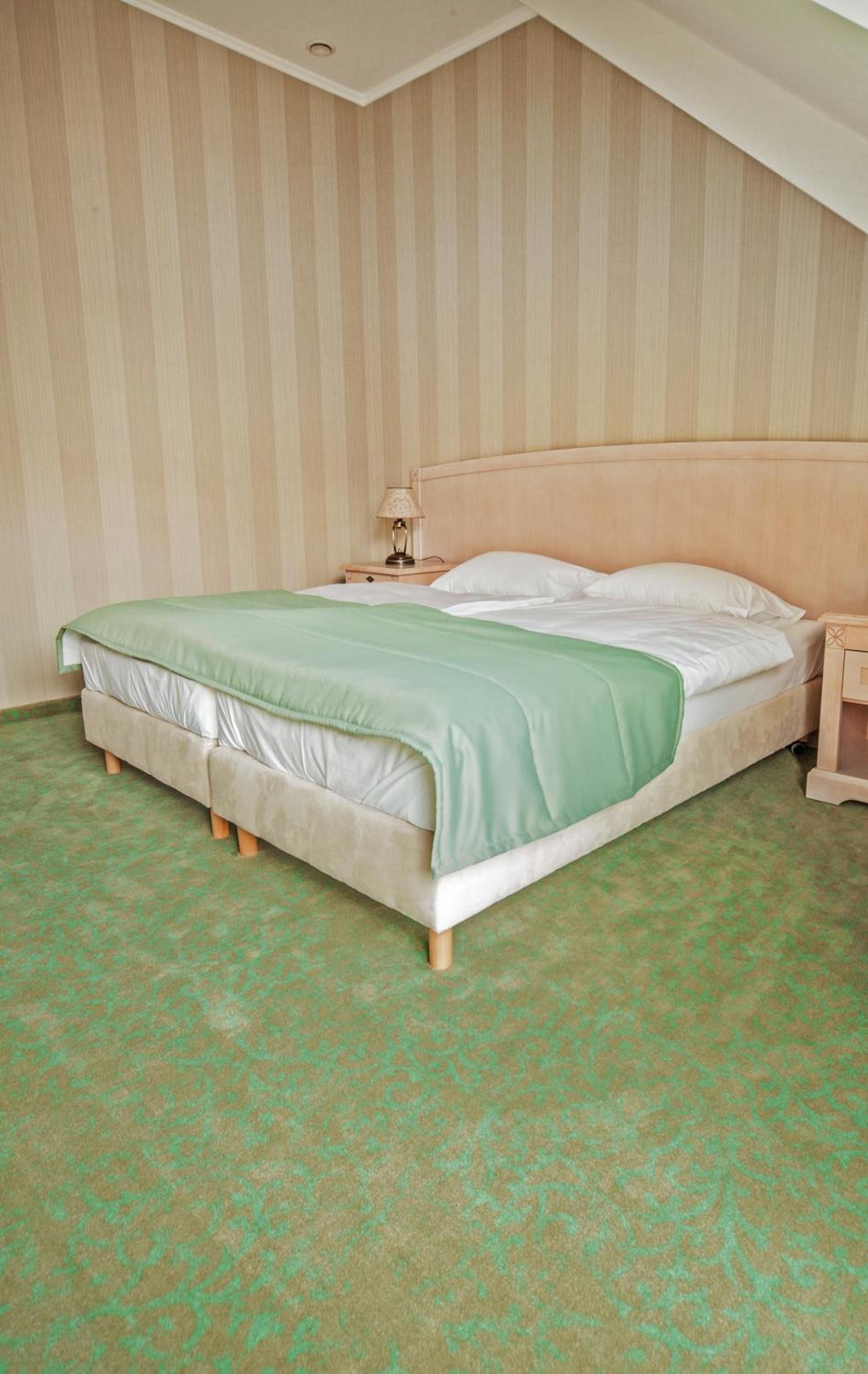 Ein Einzelzimmer mit einem Holzkopfteil, einem Nachttisch mit Lampe und einem gemusterten Teppich.