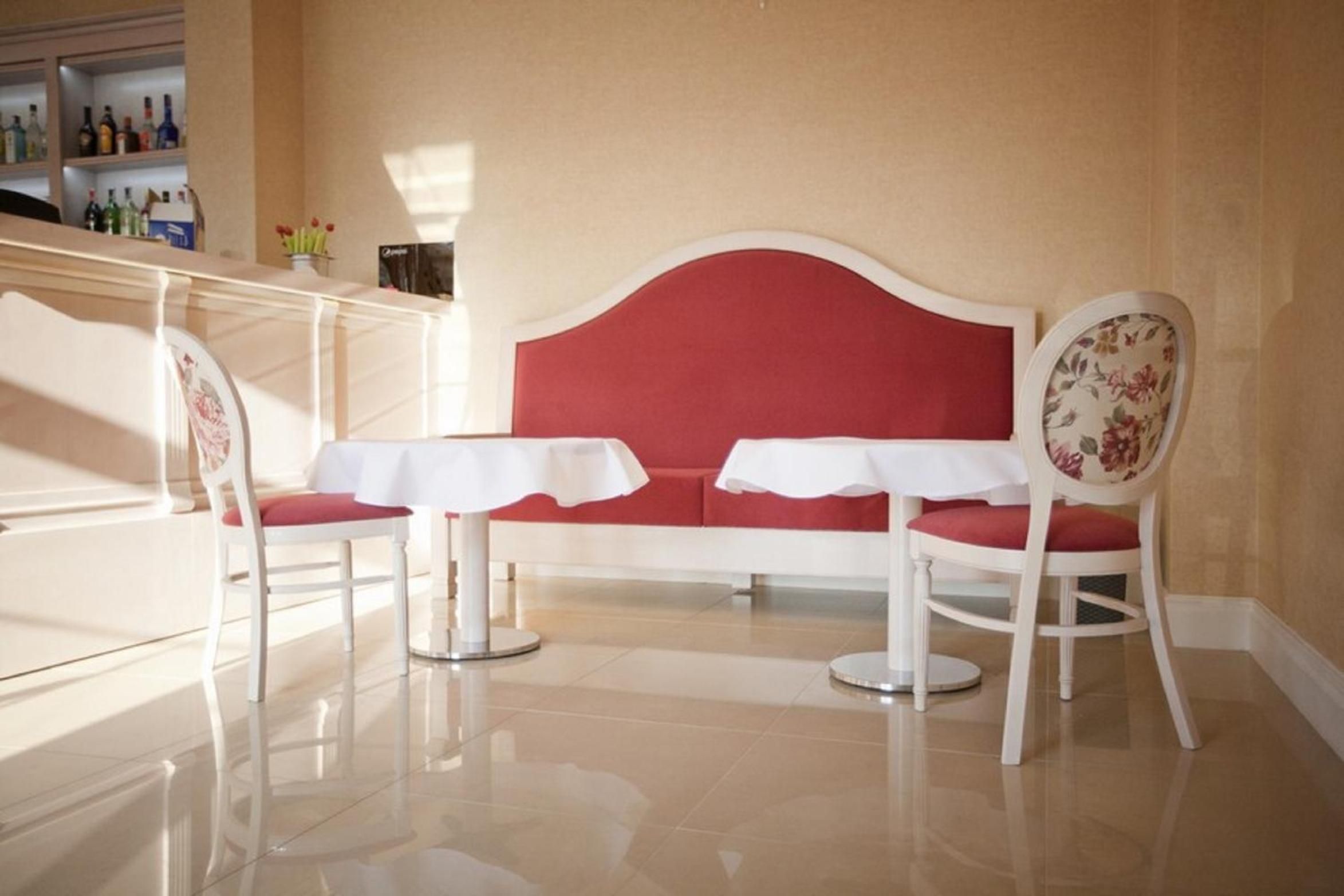 A seating area with a red sofa and two white tables, each with a chair.
