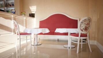 A seating area with a red sofa and two white tables, each with a chair.