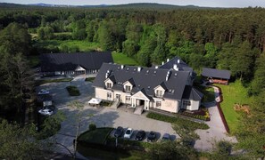 A large, multi-story building with a parking lot and several cars. - Dworek Nad Rozlewiskiem (gmina Klucze)