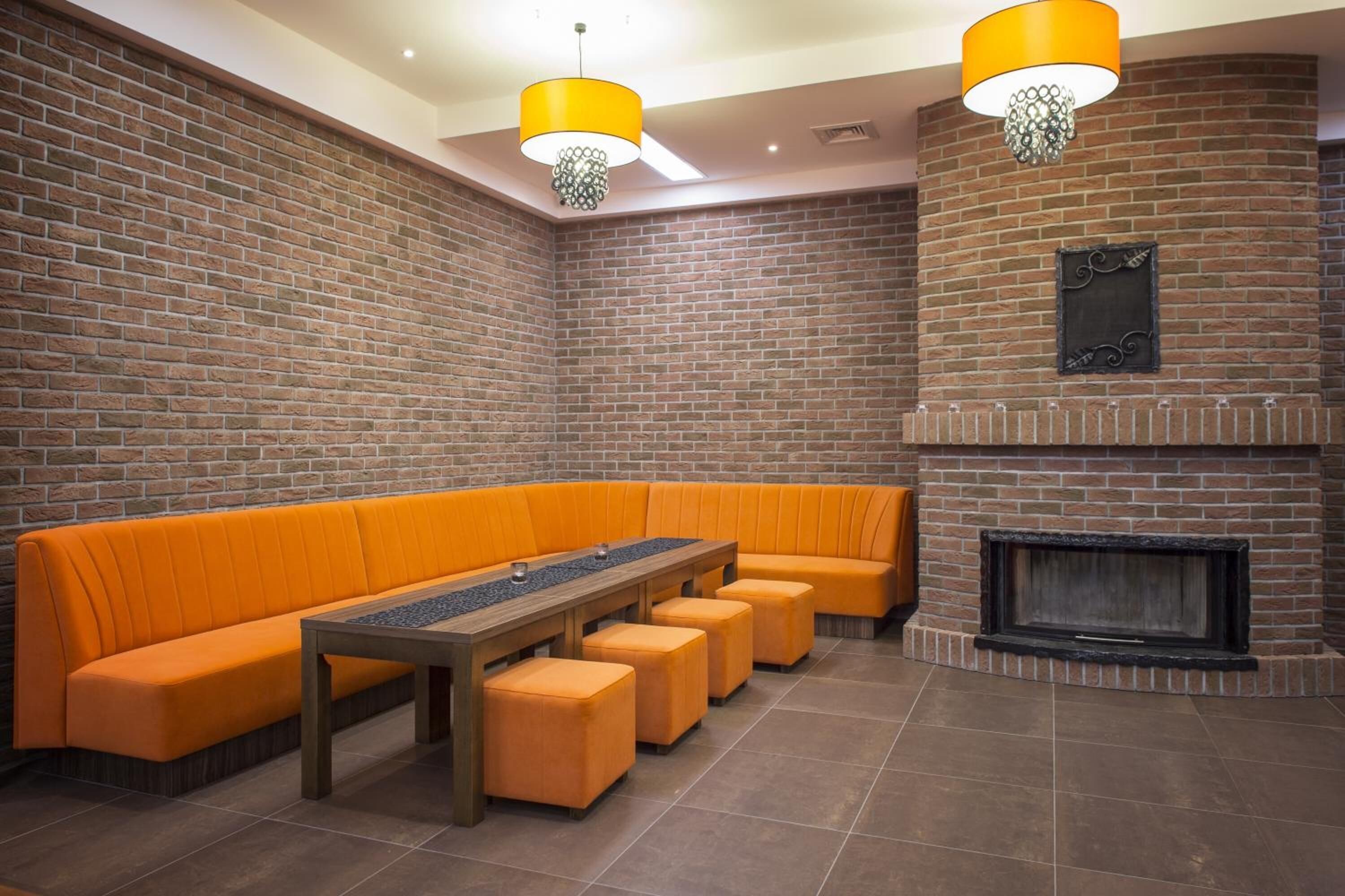 Una habitación con paredes de ladrillo, un largo banco naranja, una mesa de madera y una chimenea.
