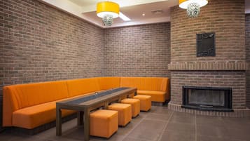 Una habitación con paredes de ladrillo, un largo banco naranja, una mesa de madera y una chimenea.