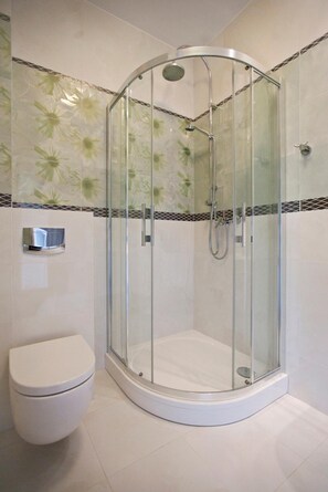 Ducha en esquina con mampara de vidrio, inodoro y azulejos decorativos.